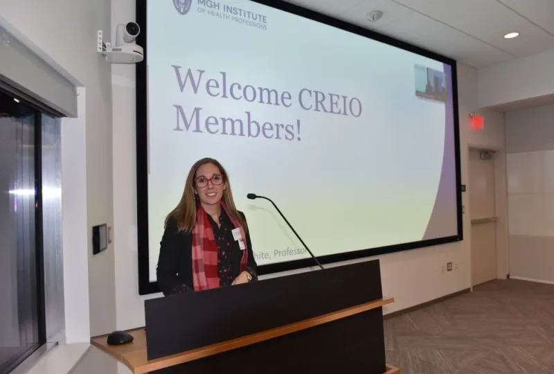 Woman at podium in front of a screen that reads Welcome CREIO members