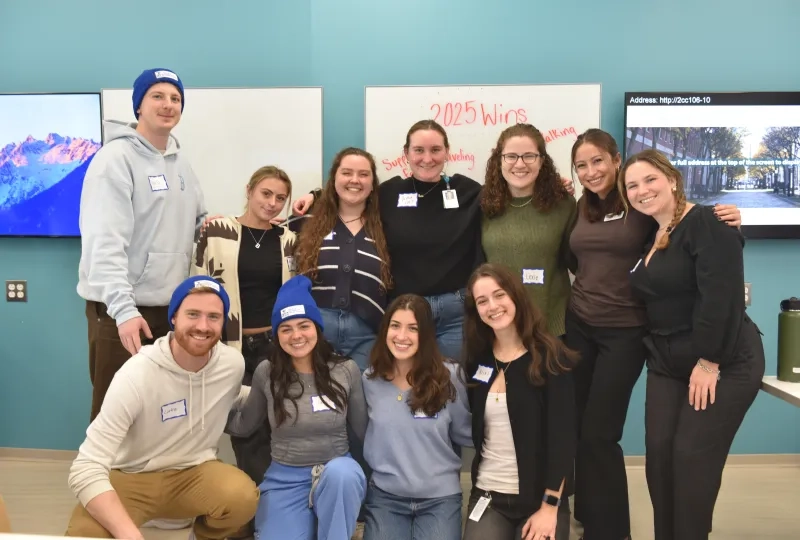 Eleven people pose in front of a board that says 2025 wins