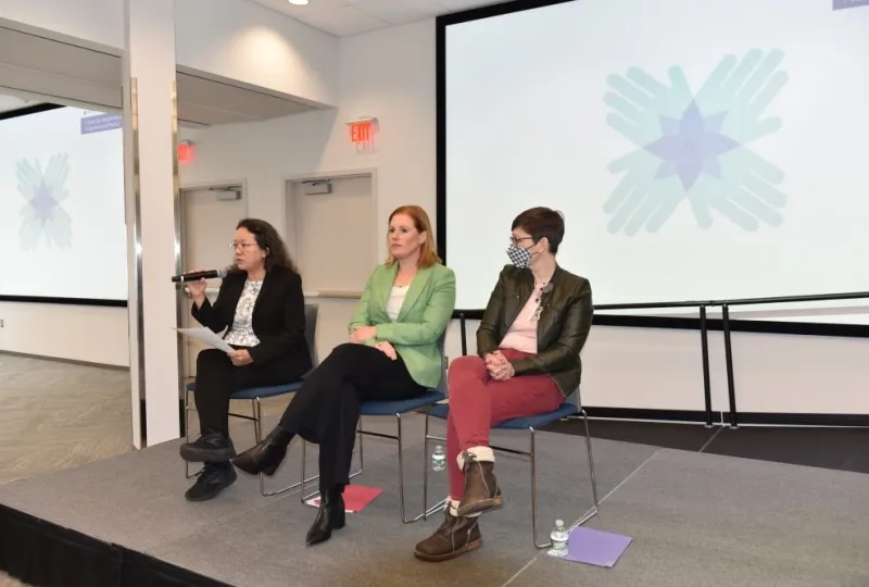 3 women sitting in chairs on a stage in front of a screen 