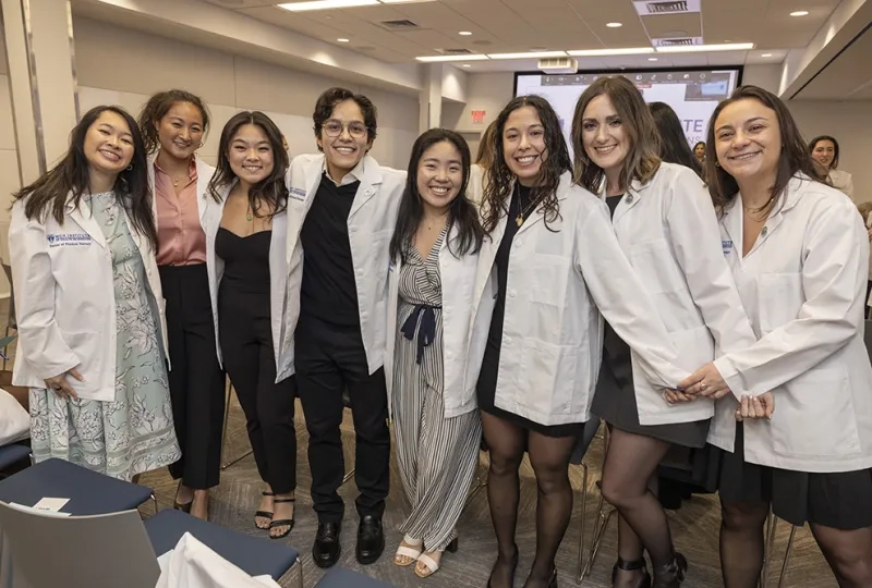 Eight people wearing white coats pose for a photo. 