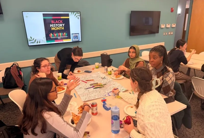 Six women sitting around a table eating and talking while two color a large sheet of paper