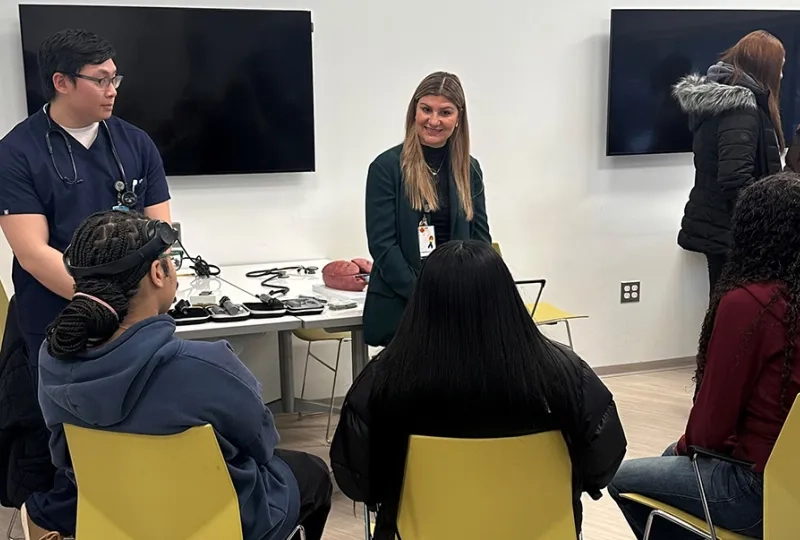 Two people stand in front of three people sitting in chairs