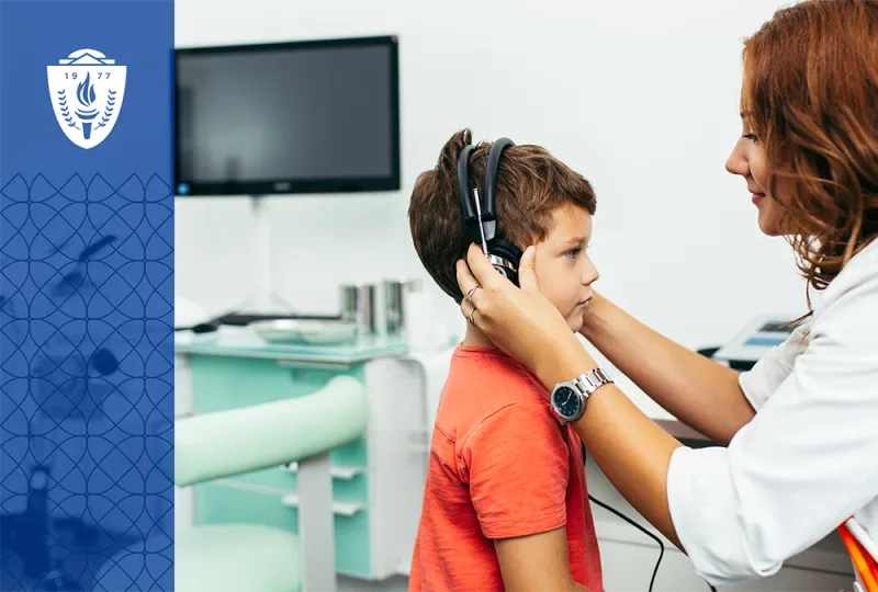 Woman wearing a lab coat putting headphone on a young boy wearing an orange T-shirt