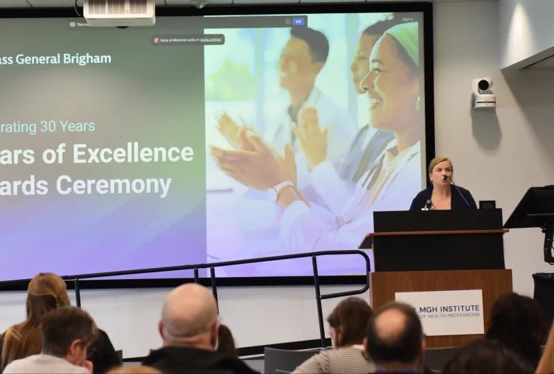 A woman talks at a podium in front of a screen