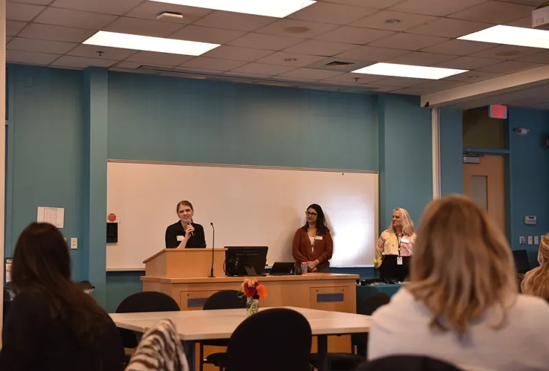 A woman speaks at a podium while two others look on