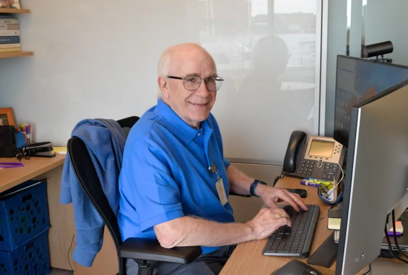 man in a blue shirt at a computer smiling 
