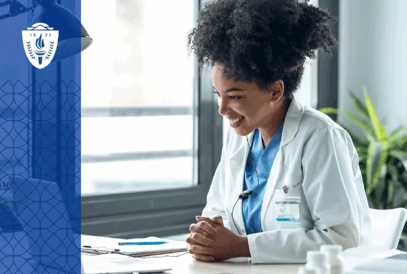 Nurse with frizzy hair wearing a lab coat sitting at a desk looking at a laptop