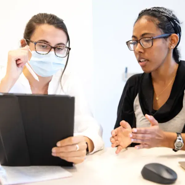 Female Physician looking at a tablet with a woman seated next to her.