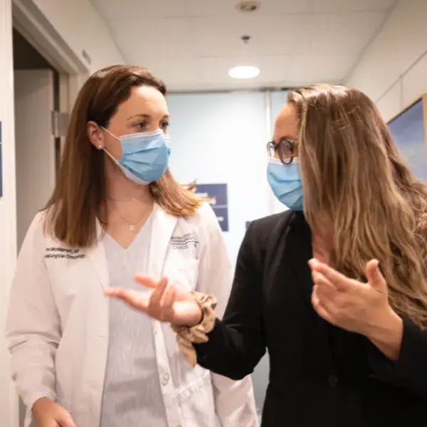 Two nurses walking down a hallway having a conversation 