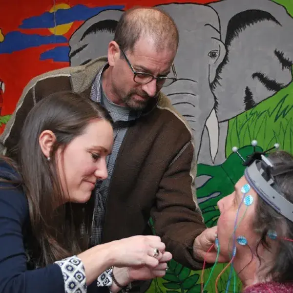 Two SFD Lab Researchers attach sensors to the head of a patient in front of a colorful painting of animals