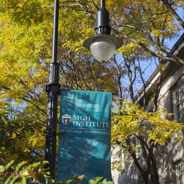 Lamp post with MGH logo flag in front of tree foliage in the sunlight