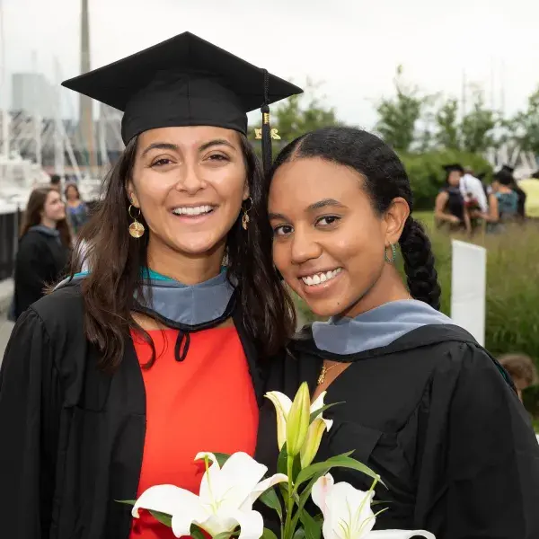 woman in red dress, black graduation cap and gown smiles with another woman in a graduation gown