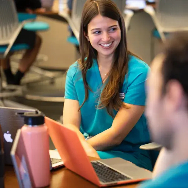 A nurse looking over her shoulder smiling in front of a laptop