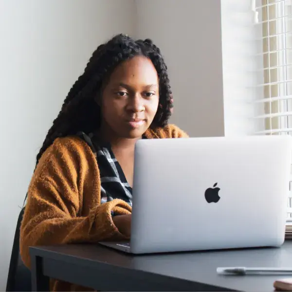 A woman using a laptop next to a window.
