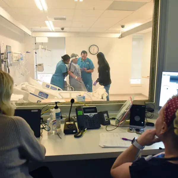 faculty observe nursing students with standardized patient through glass