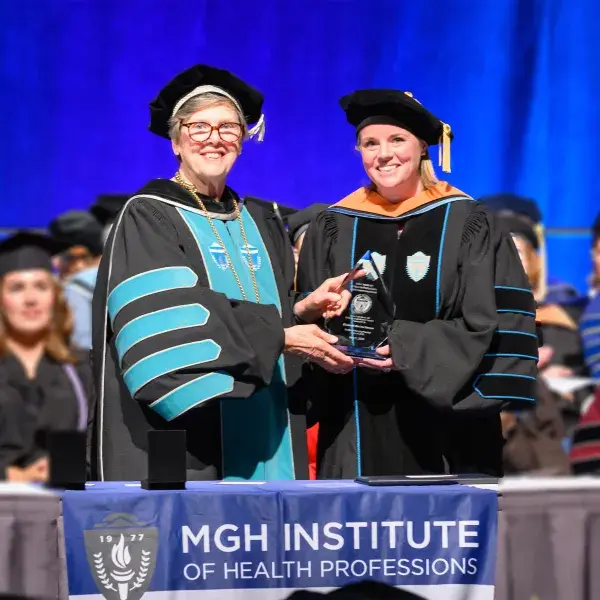 two women in graduation regalia hold a teardrop shaped crystal award
