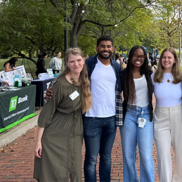 5 people standing on a brick path in front of trees huddles together