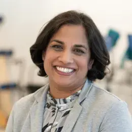 Professional portrait of an MGH IHP Doctor of Physical Therapy faculty member with a clinical setting in the background