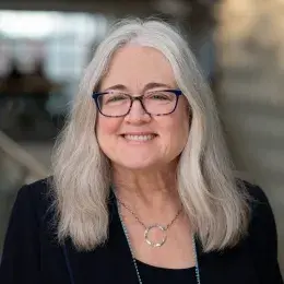 susan has shoulder length grey hair and blue tortoiseshell glasses