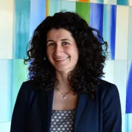 yelena wears a blue blazer and has dark wavy hair