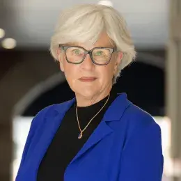 suzie has a blue blazer and black shirt on with short grey hair