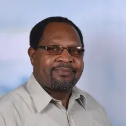 abraham wears a clay colored collared shirt and practical looking oval glasses