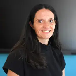 Katey has long dark hair and wears a black short sleeved top