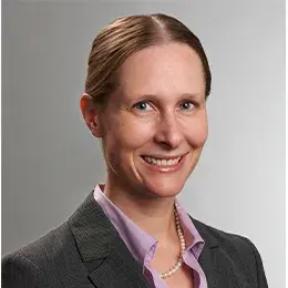 isabel has hair pulled back parted in the middle and wears a purple collared shirt under a grey blazer