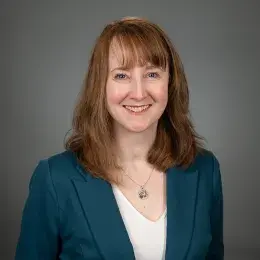 kathy wears a dark teal jacket and has strawberry blonde shoulder length hair