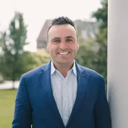 Kevin Finn is wearing a blue suit jacket and light blue shirt. He has short brown hair.