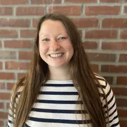 Lindsay McCabe has long brown hair is is wearing a black and white striped shirt.