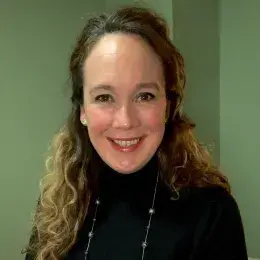 Meaghan Costello has curly, long hair and is wearing a black turtleneck