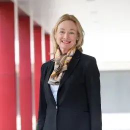 Debra Nestel has shoulder-length blonde hair and is wearing a black blazer and patterned scarf