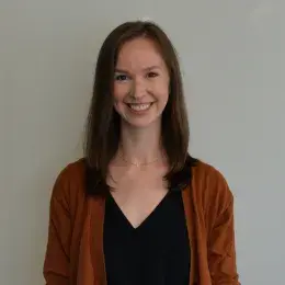 Eileen Gillan has medium brown hair and is wearing a black v-neck dress, and a orange cardigan