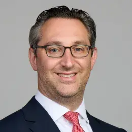 jared has glasses and a red tie with a navy jacket