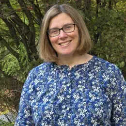 Susan Arruda has a short brown bob, glasses, and is wearing a blue floral shirt