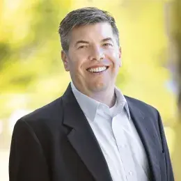 steve wears a dark suit jacket and white collared shirt in front of a bright background