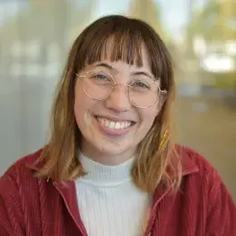 annika wears a maroon jacket and gold glasses