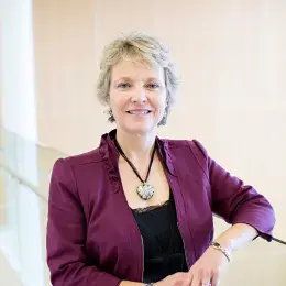 Lisa Donegan Shoaf has short light blond hair and is wearing a black shirt and dark purple jacket