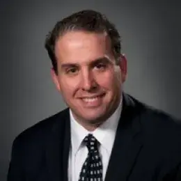 Michael Cassara has short brown hair and is wearing a black suit, with a white shirt, and black and white tie.