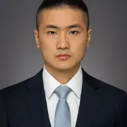 Headshot of Man wearing a white shirt, blue necktie, and black jacket against a solid dark gray background.