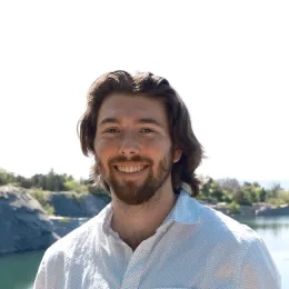 Jaryd Sullivan has shoulder length brown hair, a short beard, and is wearing a white button down.