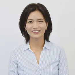 Headshot of woman with black hair standing against a solid white background wearing a blue collared shirt
