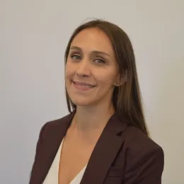 Headshot of Woman with long dark hair wearing white shirt and black jacket against a white background