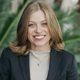 Headshot of woman with blonde hair wearing a tan shirt and black jacket