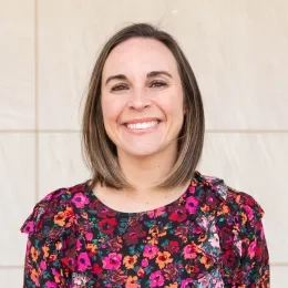 Headshot of woman with shoulder length brown hair smiling at camera and wearing floral shirt