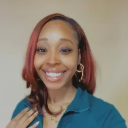 Headshot of a woman with dyed red hair smiling at the camera and wearing a blue shirt