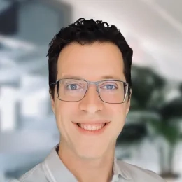 Headshot of man with short black hair wearing glasses and a gray polo shirt in front of a blurred background