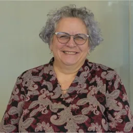 Karen has black framed glasses and grey wavy hair 