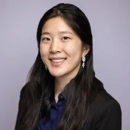 Headshot of woman with long black hair wearing a blue button-down shirt, a black jacket, and earings